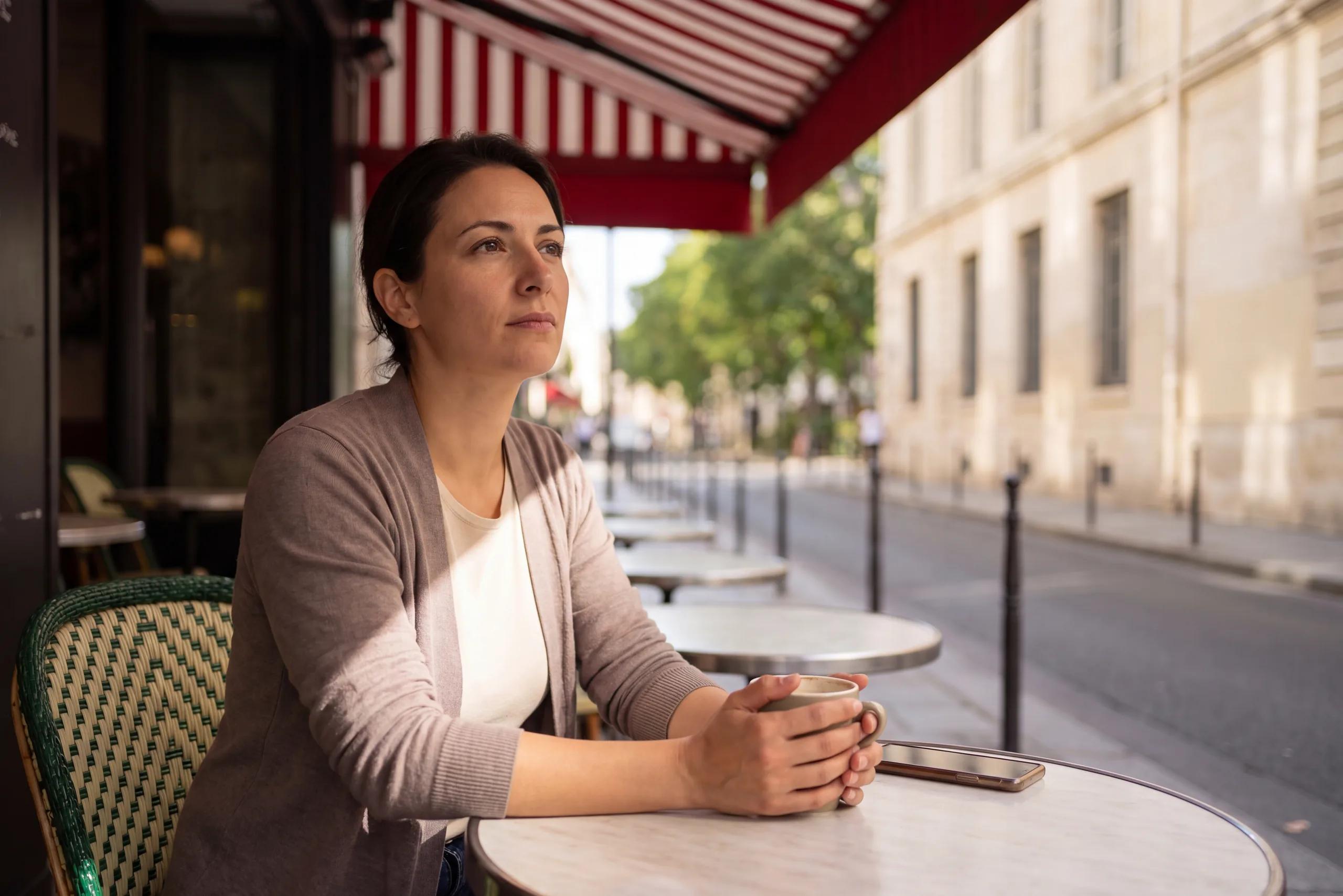 Une femme seule à la terrasse d’un café, une tasse entre les mains.