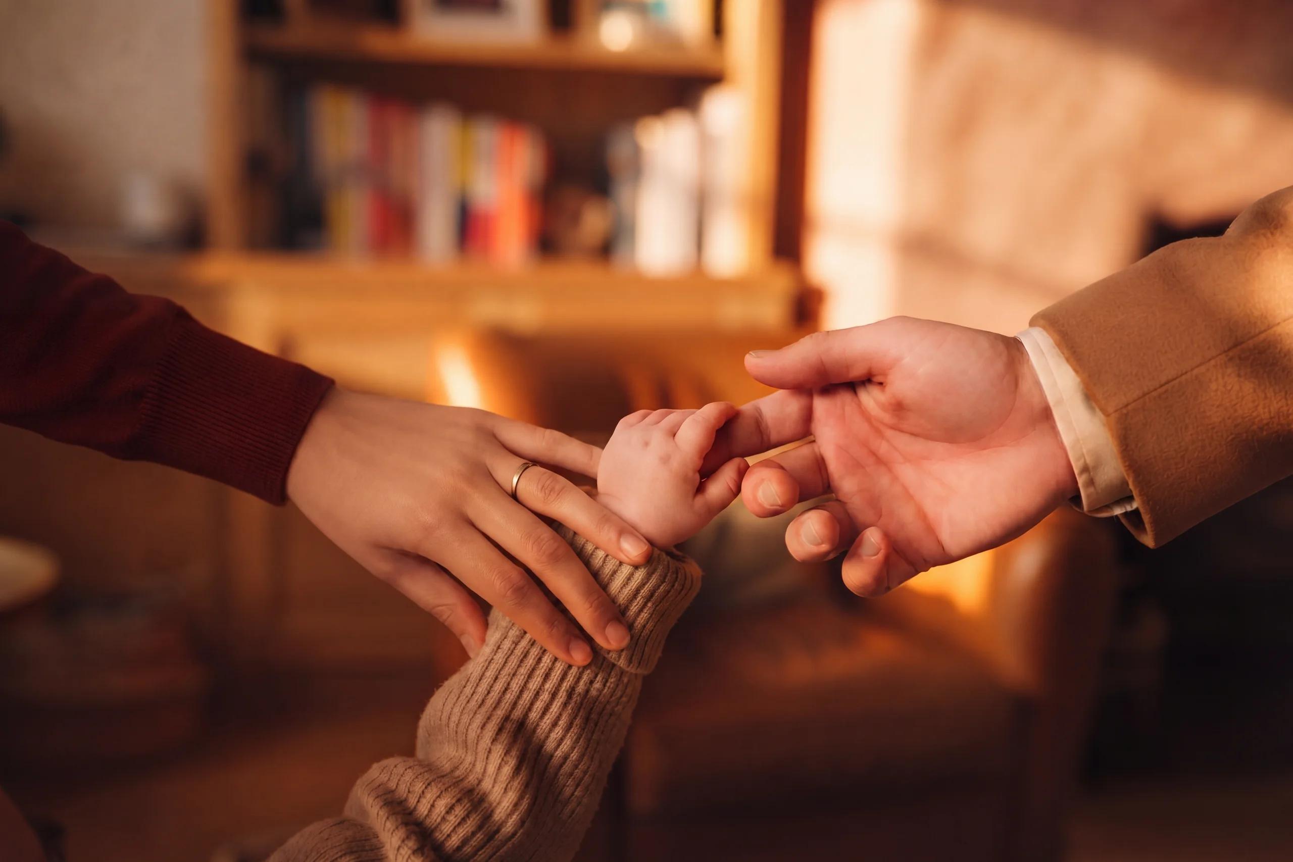 La main d’un bébé serre l’index de son père ; celle de sa mère est posée sur son poignet